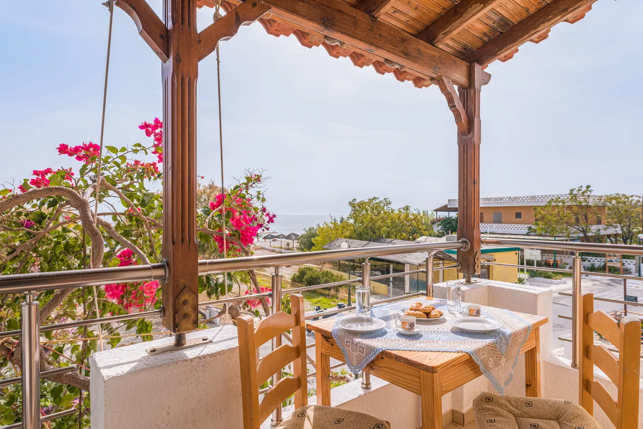 Shaded balcony under a wooden pergola with bougainvillea and a table set for breakfast