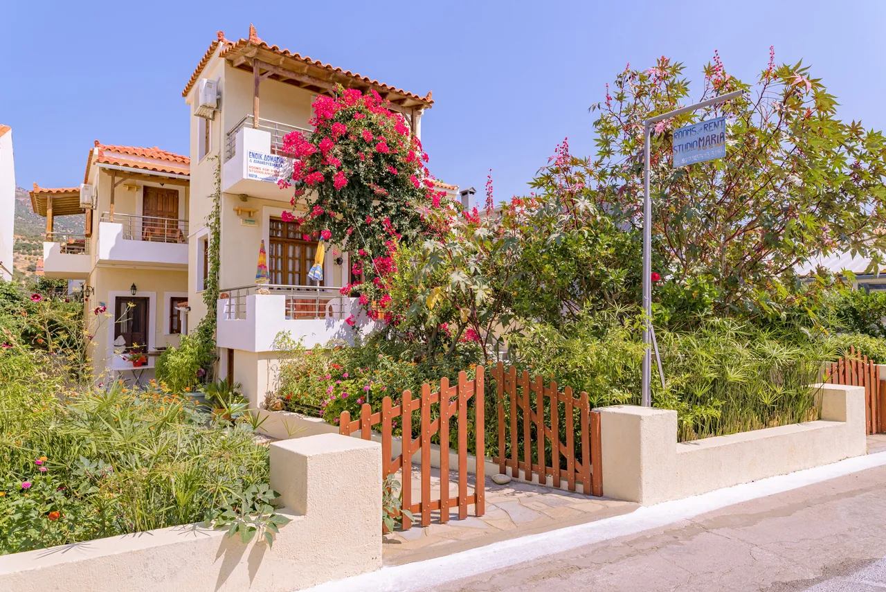 Whitewashed house with balconies behind bougainvillea and a wooden garden gate