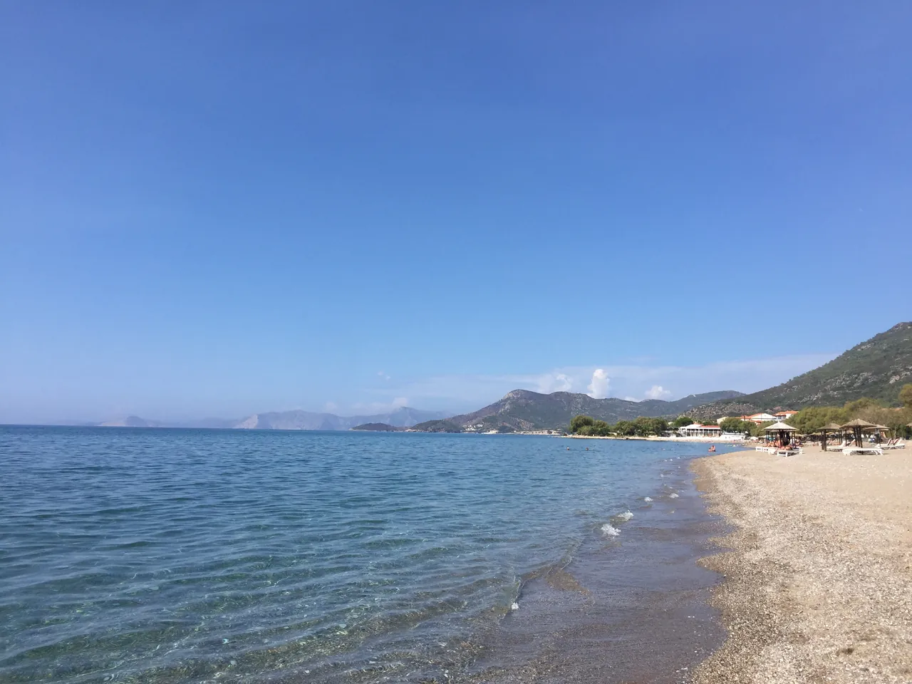 Long sandy beach with clear blue water and mountains along the coast